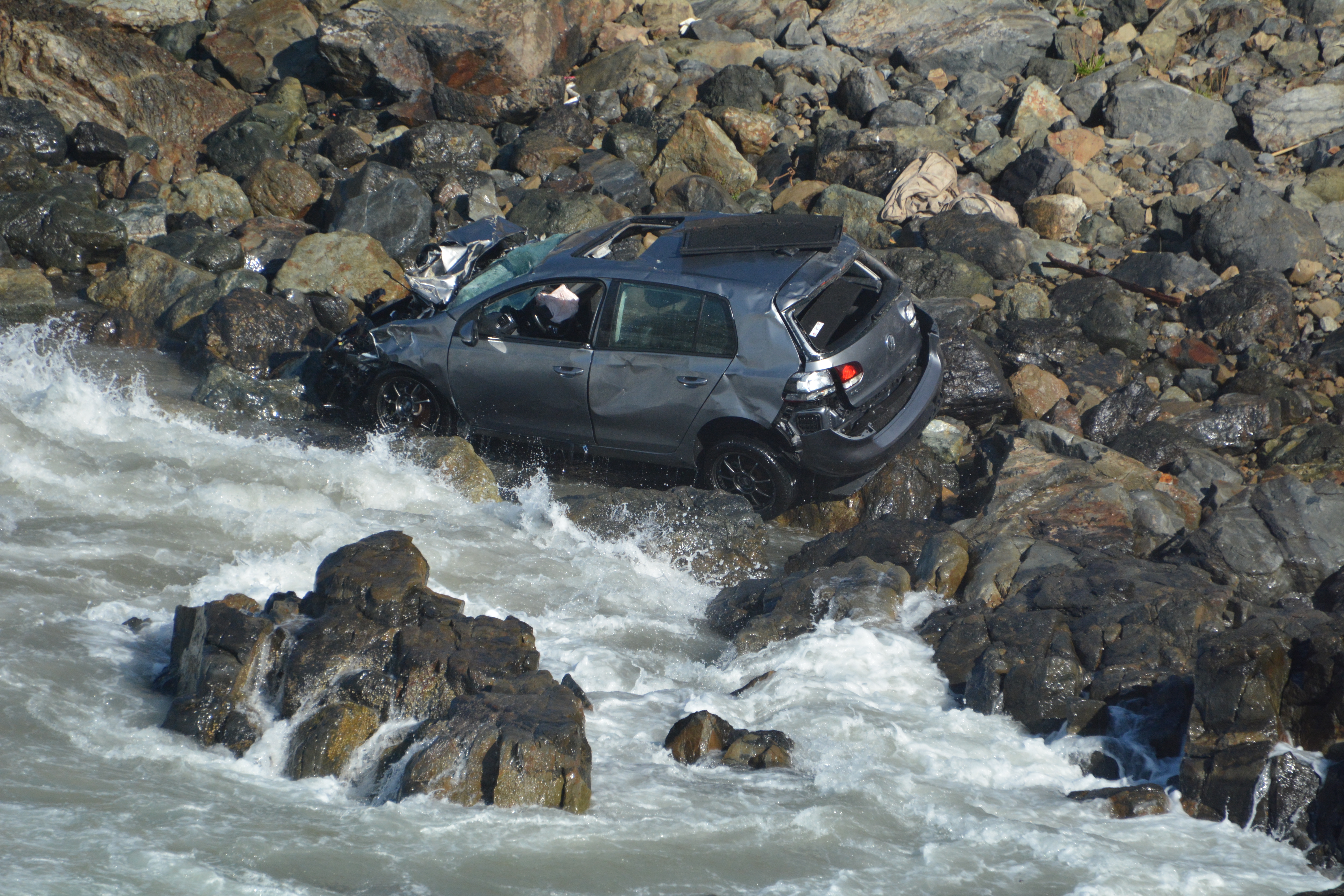 Car sits amid the rocks and waves after plunging off cliff near Stinson Beach. (CHP)