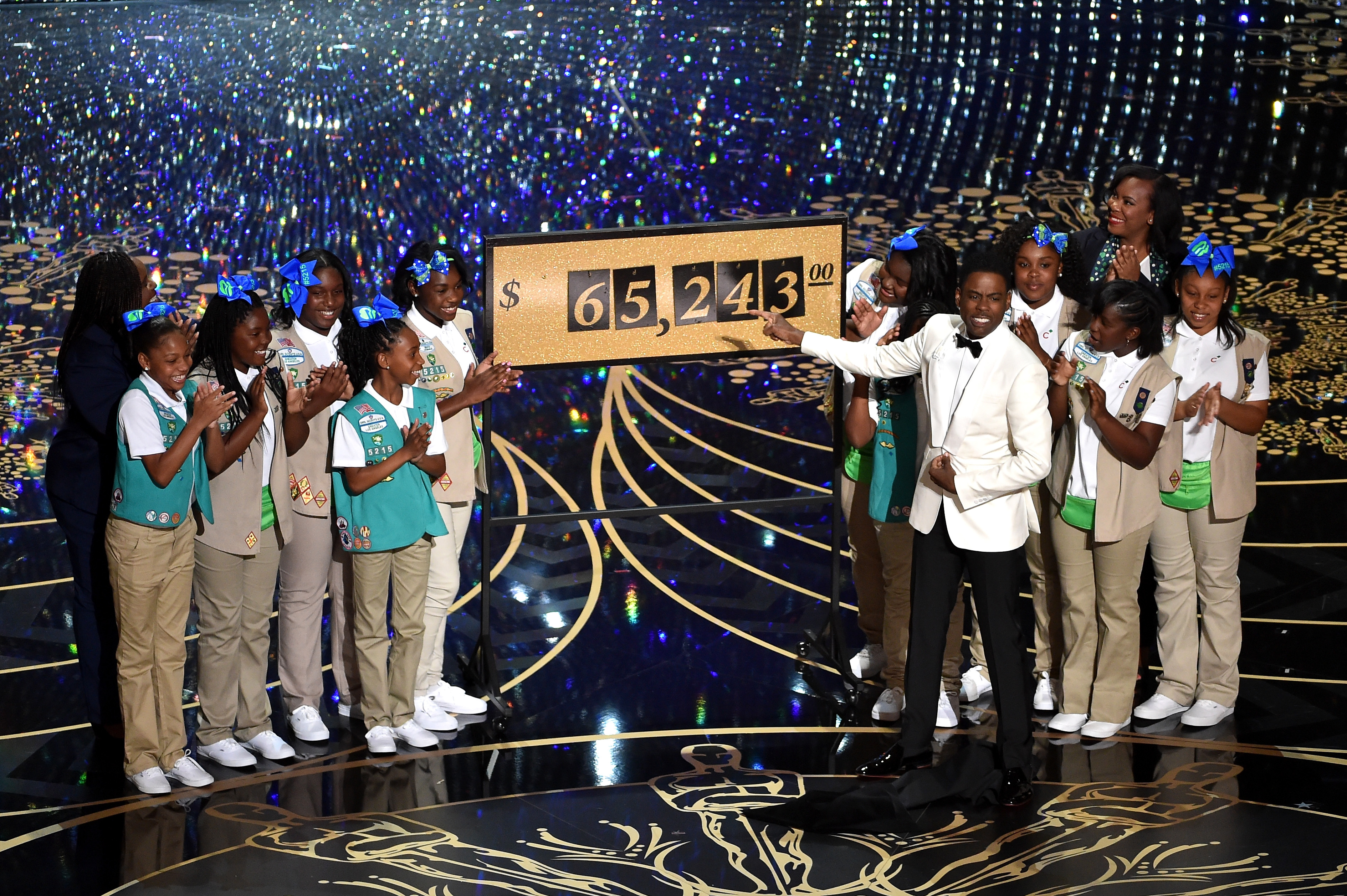 Host Chris Rock (C) presents the amount of money collected during the show by the Girl Scouts, including Rock's daughters Zahra and Lola, onstage at the 88th Annual Academy Awards.  (Photo by Kevin Winter/Getty Images)